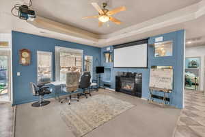 Office space with ceiling fan, a raised ceiling, and a tile fireplace