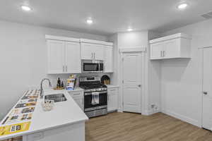 Kitchen with sink, light hardwood / wood-style flooring, white cabinets, and appliances with stainless steel finishes