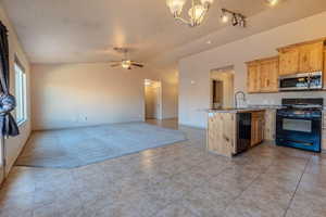 Kitchen with sink, black appliances, light brown cabinetry, vaulted ceiling, and kitchen peninsula