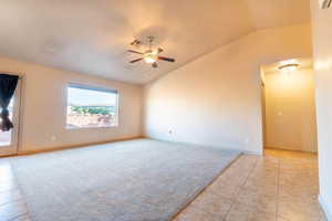 Empty room with ceiling fan, light colored carpet, and vaulted ceiling