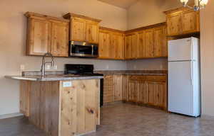 Kitchen featuring black range oven, light tile patterned floors, kitchen peninsula, and white fridge