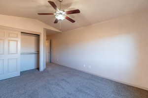 Unfurnished bedroom with ceiling fan, a closet, lofted ceiling, and carpet