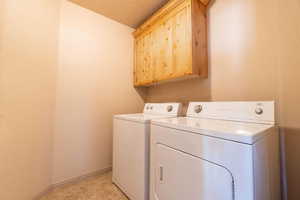 Clothes washing area featuring cabinets, washer and clothes dryer, a textured ceiling, and light tile patterned floors