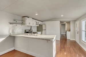 Kitchen featuring dark hardwood / wood-style floors, stainless steel fridge, kitchen peninsula, and white cabinets