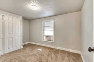 Unfurnished bedroom with cooling unit, light colored carpet, a closet, and a textured ceiling