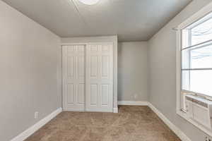 Unfurnished bedroom featuring cooling unit, light carpet, a textured ceiling, and a closet