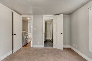 Unfurnished bedroom featuring a walk in closet, a textured ceiling, washing machine and clothes dryer, and dark carpet