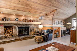 Living room featuring light colored carpet, a fireplace, wooden ceiling, and vaulted ceiling