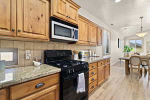 Kitchen with lofted ceiling, gas stove, light stone counters, tasteful backsplash, and light wood-type flooring