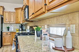 Kitchen with light stone counters, black range oven, light hardwood / wood-style flooring, fridge, and backsplash