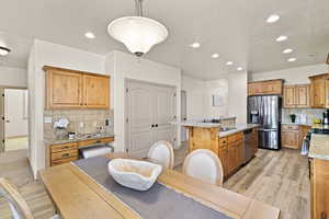 Kitchen featuring light stone counters, appliances with stainless steel finishes, an island with sink, pendant lighting, and light hardwood / wood-style floors