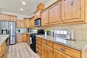 Kitchen with stainless steel appliances, light stone countertops, light hardwood / wood-style floors, and decorative backsplash