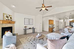 Living room featuring a tiled fireplace, lofted ceiling, and ceiling fan