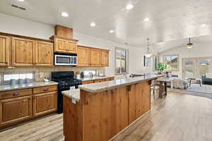 Kitchen featuring decorative light fixtures, black range with gas stovetop, a center island, light stone counters, and light wood-type flooring