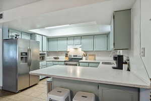 Kitchen featuring light tile patterned flooring, appliances with stainless steel finishes, sink, backsplash, and kitchen peninsula