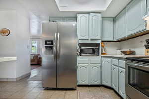 Kitchen with a raised ceiling, appliances with stainless steel finishes, light tile patterned floors, and decorative backsplash