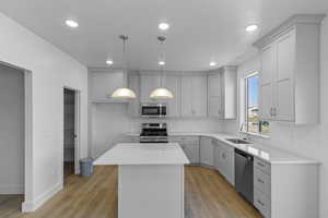 Kitchen with gray cabinetry, a center island, hanging light fixtures, stainless steel appliances, and light floors