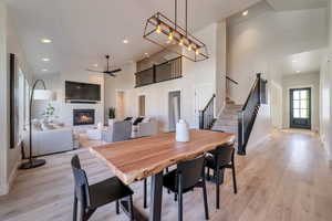 Dining space with ceiling fan with notable chandelier, high vaulted ceiling, and light hardwood / wood-style flooring