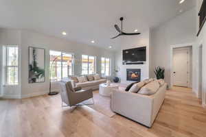 Living room with high vaulted ceiling, ceiling fan, and light wood-type flooring