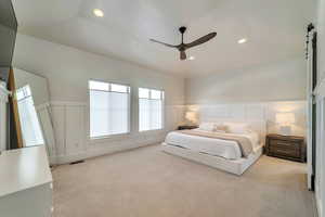 Bedroom with ceiling fan, a barn door, and light carpet