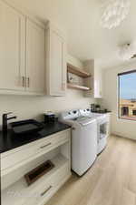 Laundry area with sink, light hardwood / wood-style floors, cabinets, and independent washer and dryer