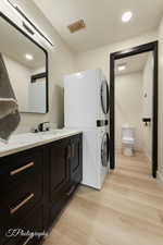 Bathroom featuring vanity, hardwood / wood-style floors, stacked washer and clothes dryer, and toilet