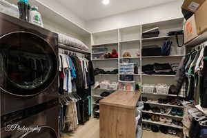 Walk in closet with stacked washer and dryer and light wood-type flooring