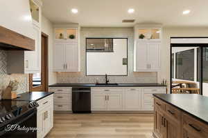 Kitchen featuring sink, light hardwood / wood-style flooring, tasteful backsplash, black appliances, and white cabinets