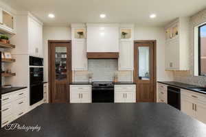 Kitchen featuring tasteful backsplash, premium range hood, white cabinets, and black appliances