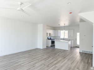 Kitchen featuring a kitchen island, white cabinets, hanging light fixtures, stainless steel appliances, and light wood-type flooring