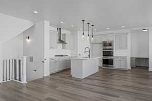 Kitchen with sink, pendant lighting, stainless steel appliances, a kitchen island with sink, and wall chimney range hood