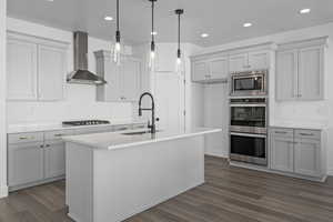 Kitchen featuring a center island with sink, hanging light fixtures, sink, and wall chimney range hood