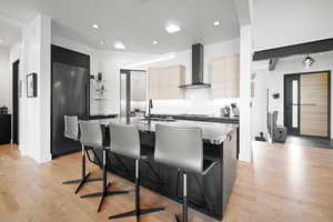 Kitchen with wall chimney range hood, sink, a breakfast bar, paneled fridge, and an island with sink