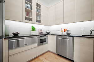 Kitchen featuring stainless steel appliances, sink, light wood-type flooring, and dark stone counters