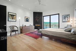 Bedroom featuring light hardwood / wood-style flooring, access to outside, a large fireplace, and ceiling fan