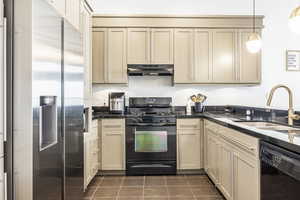 Kitchen featuring cream cabinetry, dark tile patterned floors, black appliances, and sink