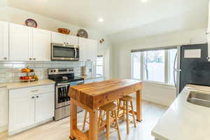 Kitchen featuring lofted ceiling, white cabinetry, tasteful backsplash, stainless steel appliances, and light hardwood / wood-style floors