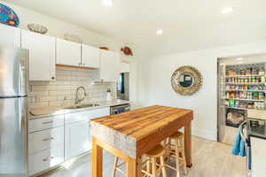 Kitchen featuring appliances with stainless steel finishes, tasteful backsplash, white cabinetry, sink, and light hardwood / wood-style flooring