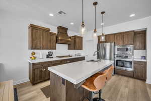 Kitchen with a breakfast bar, sink, appliances with stainless steel finishes, custom range hood, and a kitchen island with sink