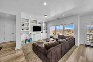 Living room with built in features, a textured ceiling, and light wood-type flooring