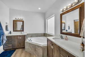 Bathroom with a relaxing tiled tub, hardwood / wood-style floors, and vanity