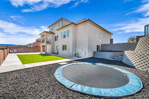 Rear view of house featuring a lawn, a trampoline, a patio area, ac unit, and a balcony