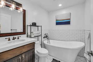 Bathroom with vanity, tile walls, a tub, and toilet