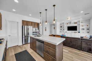 Kitchen with sink, hanging light fixtures, light wood-type flooring, an island with sink, and stainless steel appliances