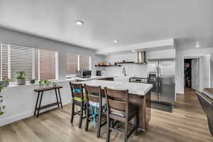 Kitchen featuring stainless steel appliances, a breakfast bar, light hardwood / wood-style flooring, and wall chimney exhaust hood