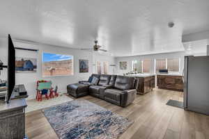 Living room with ceiling fan, a wall mounted air conditioner, a textured ceiling, and light wood-type flooring