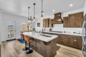 Kitchen with an island with sink, sink, a kitchen breakfast bar, hanging light fixtures, and custom range hood