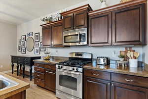 Kitchen with stainless steel appliances, a textured ceiling, dark brown cabinets, and light wood-type flooring