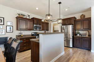 Kitchen featuring pendant lighting, appliances with stainless steel finishes, a center island, and light wood-type flooring