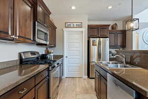 Kitchen featuring sink, stainless steel appliances, dark brown cabinetry, light hardwood / wood-style floors, and decorative light fixtures